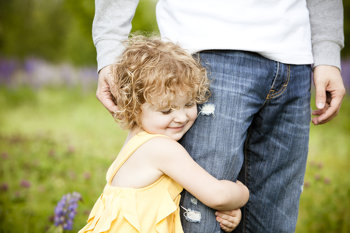 "Beautiful girl hugging her father's leg. Father is gently embracing her head. Good spring, Easter, summer image. Very shallow depth of field."